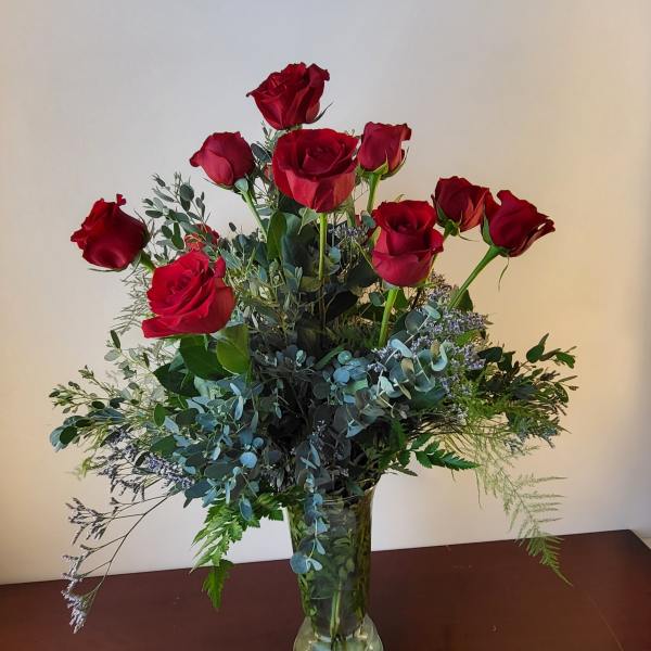 Red roses arranged in a clear glass vase with mixed greenery