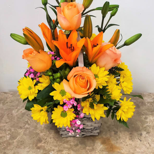 Orange roses and lilies in a basket with yellow daisies