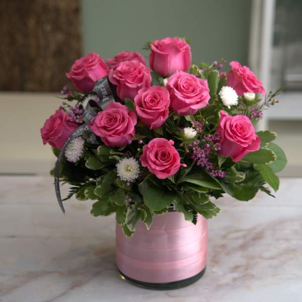 Low arrangement of hot pink roses with white accents in a pink-wrapped glass cylinder vase