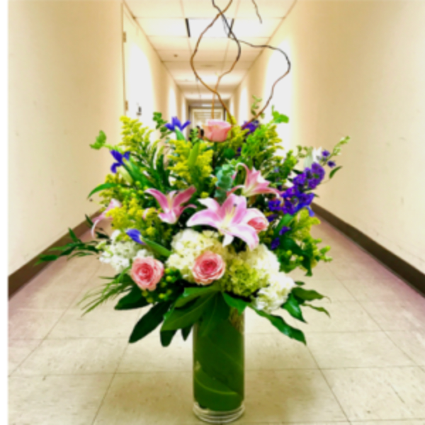 Tall mixed flower arrangement in a green vase with pink lilies and roses