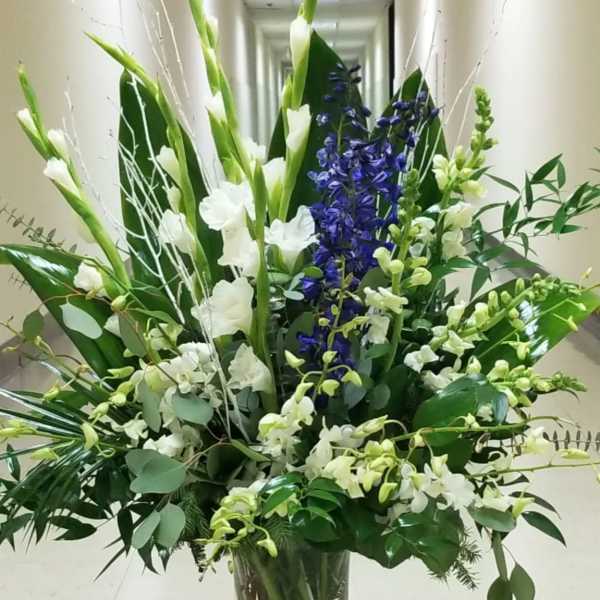 Tall floral arrangement in a clear glass vase with white and blue blooms