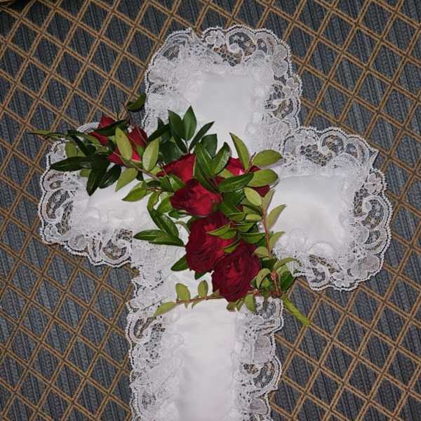 Red roses and greenery arranged on a white lace cross