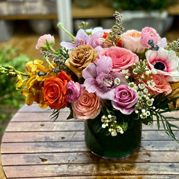Mixed bouquet of pink, peach, and orange flowers in a dark glass vase
