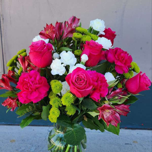 Bouquet of pink roses, white blooms, and green button mums in a glass vase