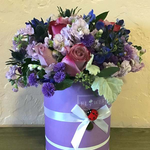 Pink and purple flower arrangement in a lavender hat box with a white ribbon