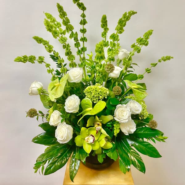 White roses and green orchids in a black vase with tall green spikes.