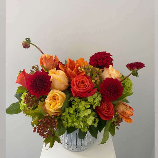Mixed bouquet of red, orange, and yellow flowers in a silver vase
