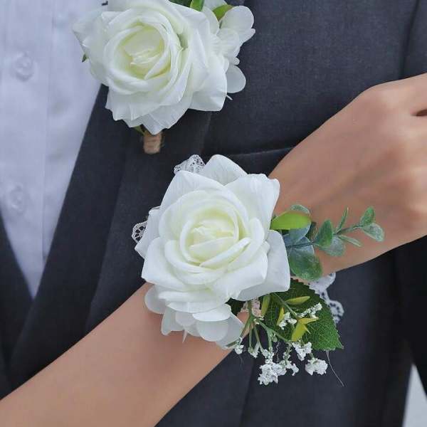 Matching white rose boutonniere and wrist corsage with small white filler flowers on formal attire.