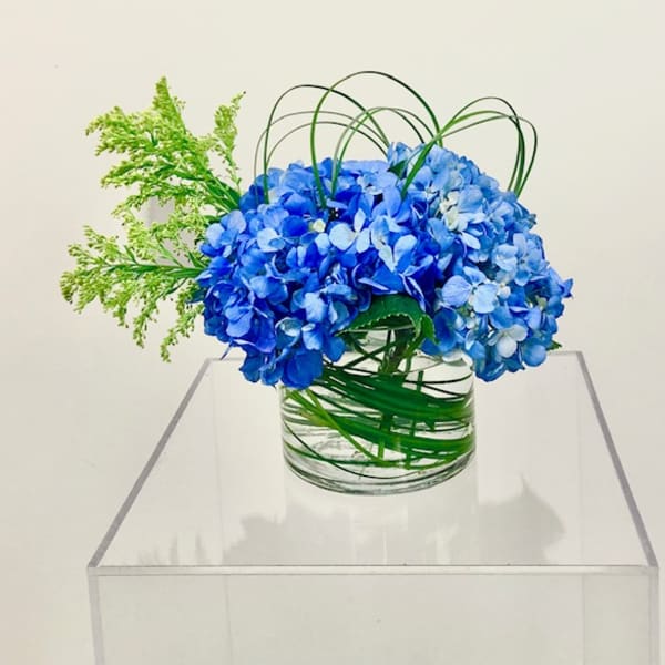Blue hydrangea arrangement in a clear glass vase with green decorative loops