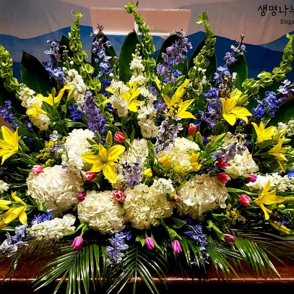 Large altar arrangement of yellow lilies, white hydrangeas and blue flowers in a fan-shaped display