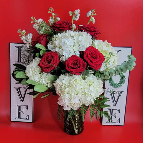 Red roses and white hydrangeas in a glass vase with decorative letters behind