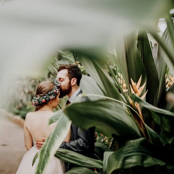 Bride and groom kissing among tropical plants with a floral crown