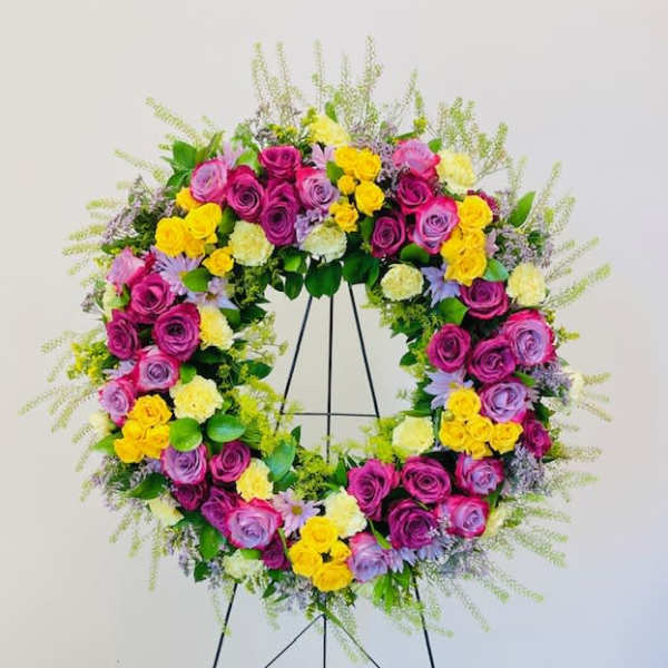 Circular floral wreath of pink, purple, and yellow roses on a stand