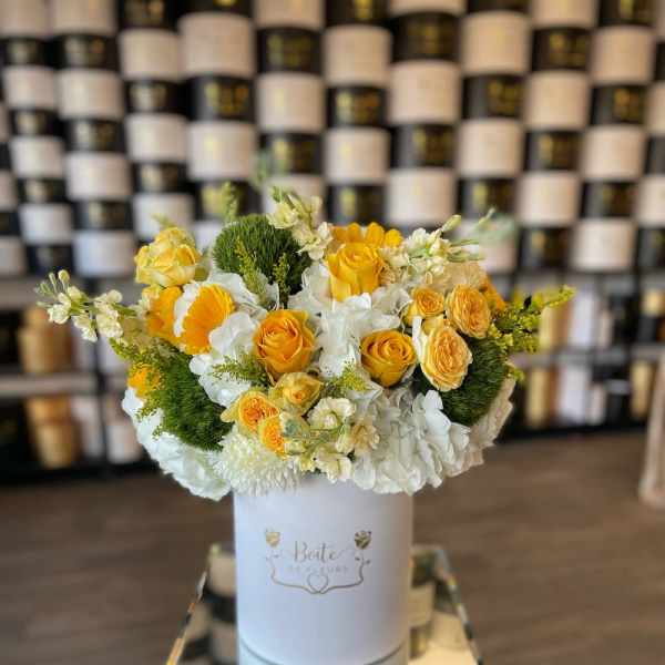 Yellow and white floral arrangement in a white hat box