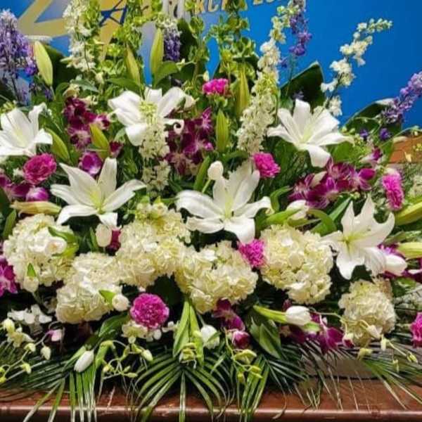 Large white and purple altar-style flower arrangement with lilies, hydrangeas, and orchids