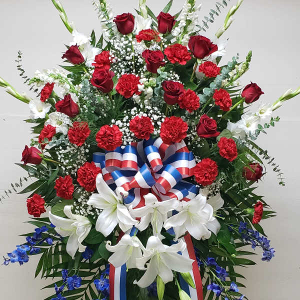 Tall red, white, and blue standing spray with roses, carnations, lilies, and ribbon on an easel