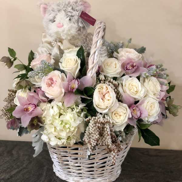 White wicker basket with pastel roses, orchids, and a plush cat