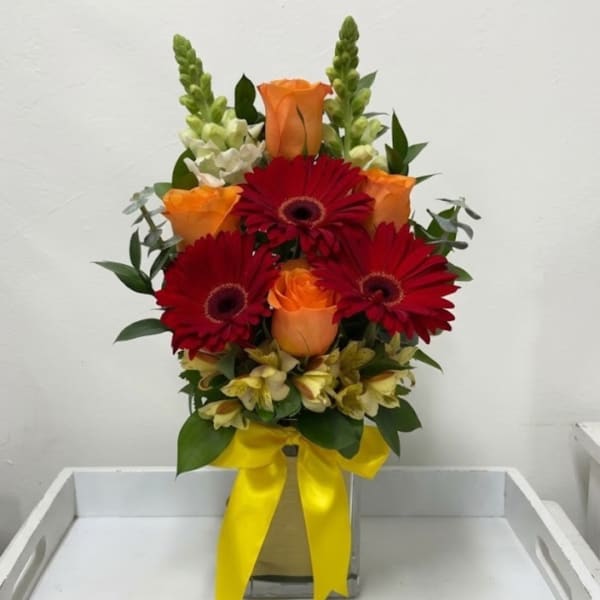 Orange roses and red gerbera daisies in a vase with a yellow ribbon
