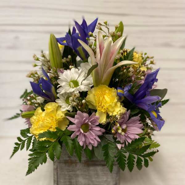 Mixed bouquet in a gray wooden box with blue, yellow, white, and lavender flowers