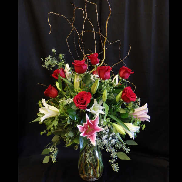 Red roses and white lilies in a glass vase with tall curly branches