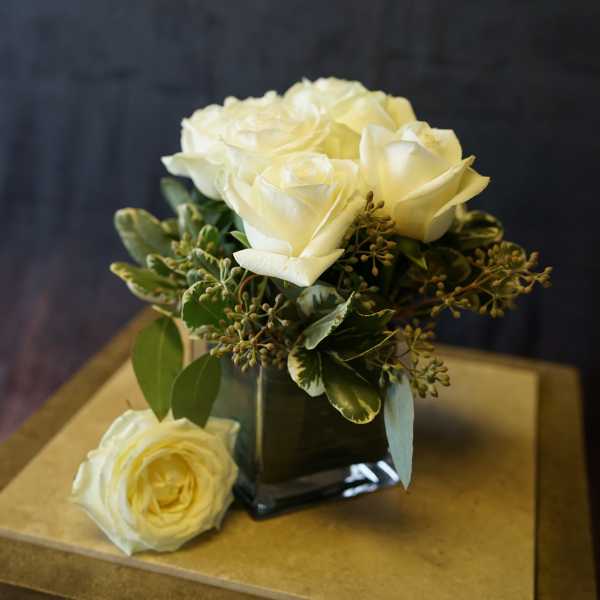 White roses arranged in a square glass vase with greenery