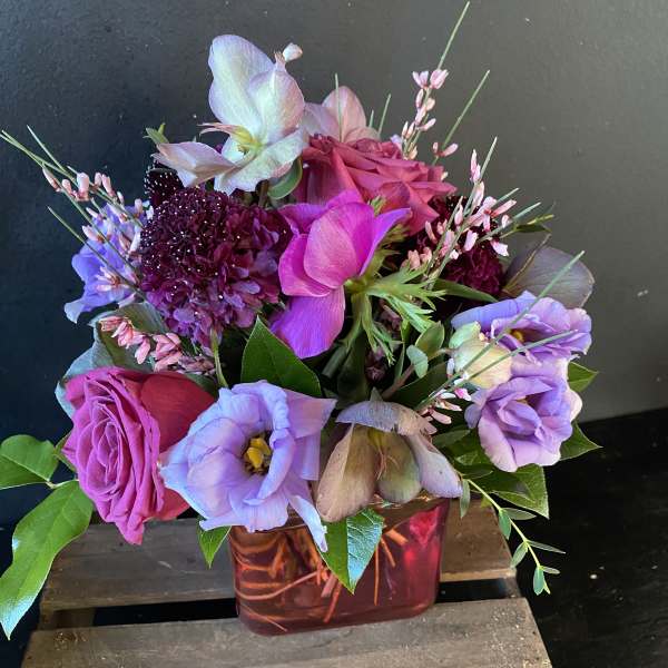 Mixed bouquet of pink, purple, and lavender flowers in a red glass vase