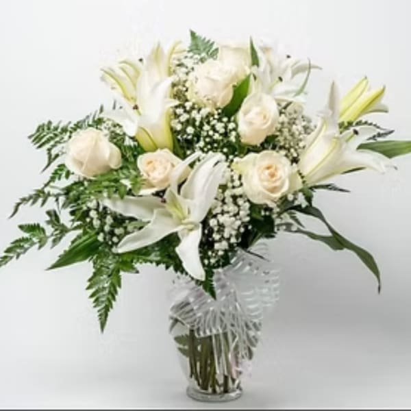White lilies and cream roses arranged in a clear glass vase