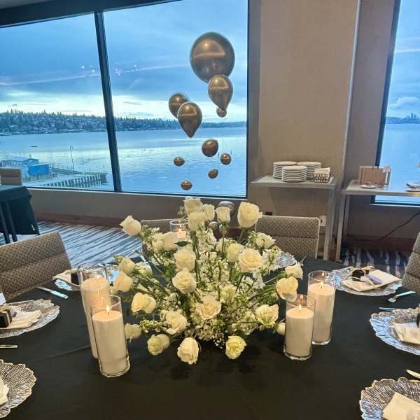 White rose centerpiece on a black table with candles and place settings