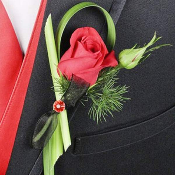 Red rose boutonniere with green accents pinned to a black suit
