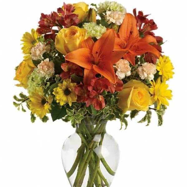 Bouquet of orange lilies, yellow roses, and mixed flowers in a clear glass vase