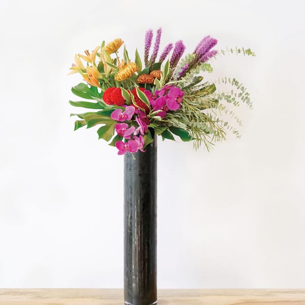 Tropical bouquet with orchids and orange blooms in a tall black vase
