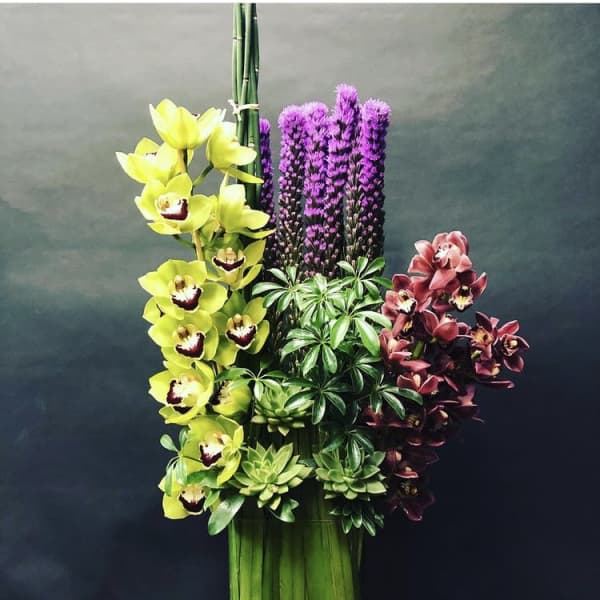 Arrangement of yellow and burgundy orchids with purple spikes and green foliage