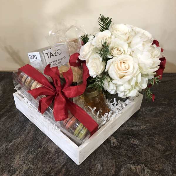 Gift basket with white roses, tea, cookies, and a red ribbon