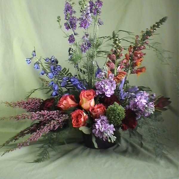 Tall mixed bouquet with orange roses and purple flowers in a black vase