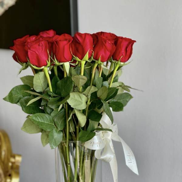 Tall bouquet of red roses in a clear glass vase with a white ribbon