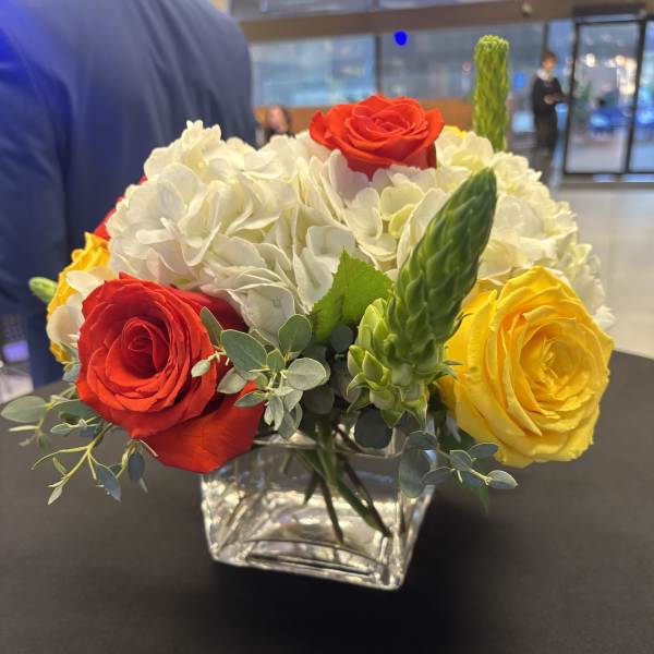 Red, yellow, and white roses in a clear square vase
