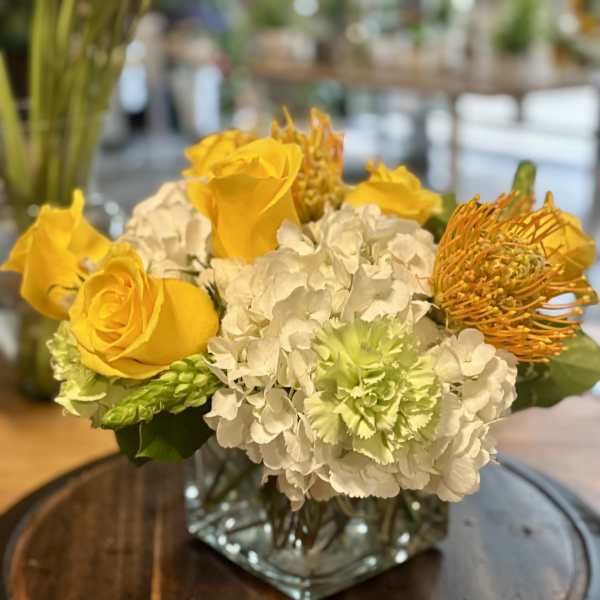 Yellow roses and white hydrangeas in a square glass vase