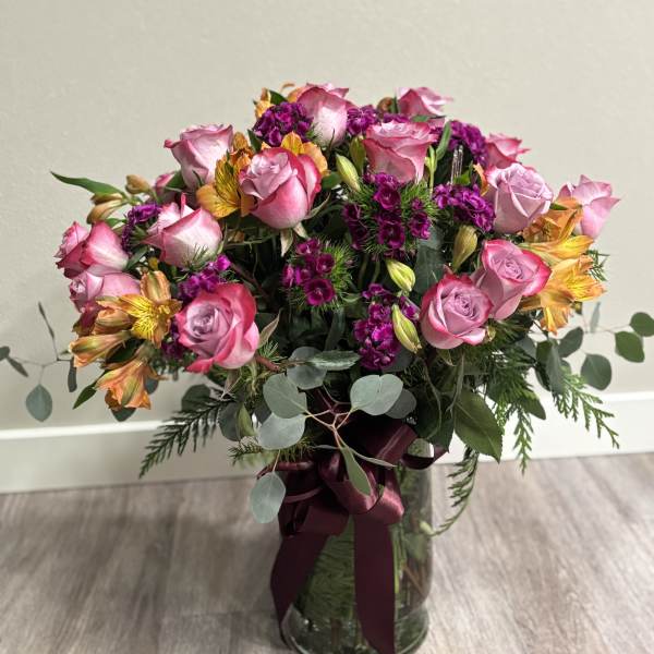 Pink roses and purple flowers in a glass vase with a burgundy ribbon