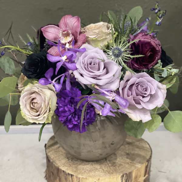 Purple and cream roses with orchids in a round vase