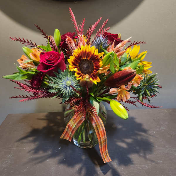 Mixed bouquet in a glass vase with sunflowers, roses, and lilies