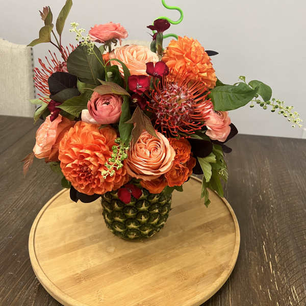 Orange and pink floral arrangement in a pineapple vase