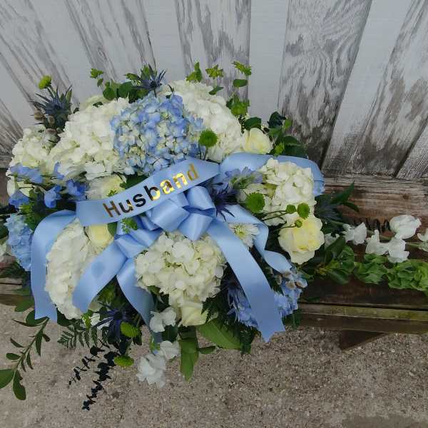 White and blue floral arrangement with a blue ribbon labeled Husband