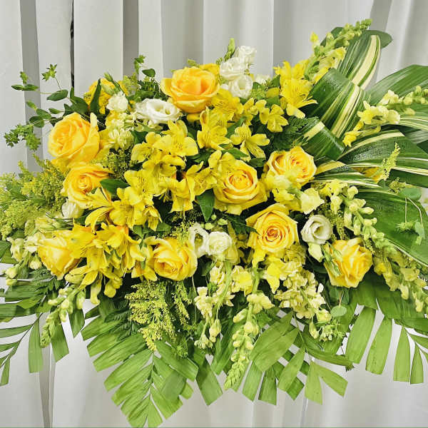 Yellow roses and mixed yellow-white flowers in a large arrangement with broad green leaves.