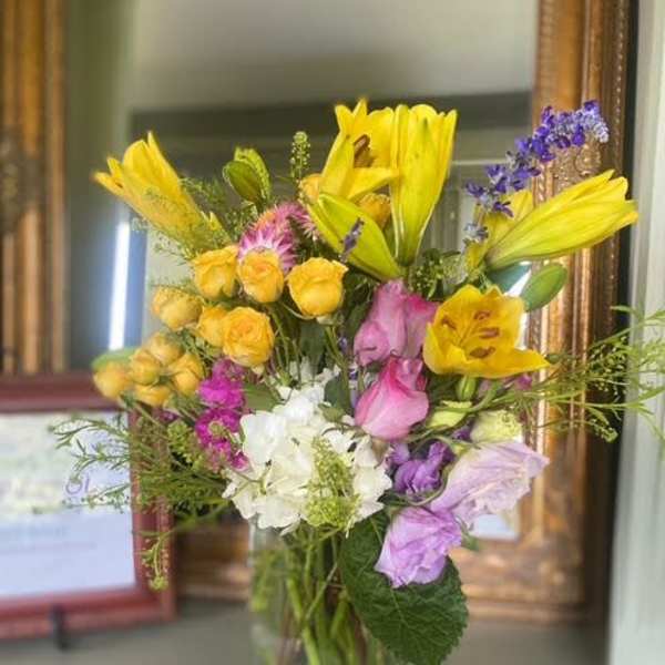 Bouquet of yellow lilies, roses, and purple flowers in a clear glass vase