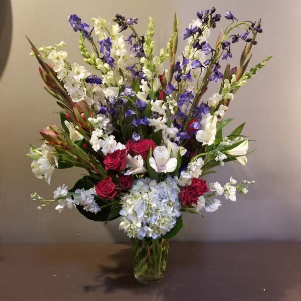 Tall bouquet of red roses, white lilies, blue flowers, and hydrangea in a glass vase