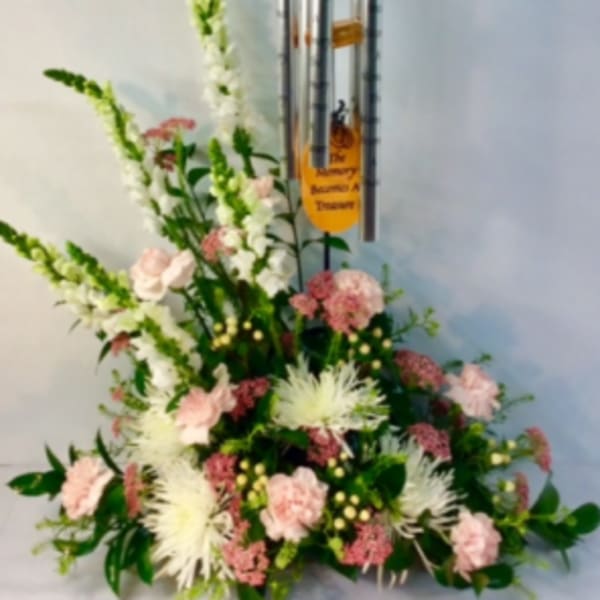 Standing floral arrangement with pink and white flowers beneath silver wind chimes