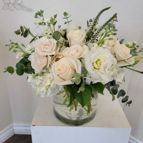 Cream roses and white blooms arranged in a clear glass vase