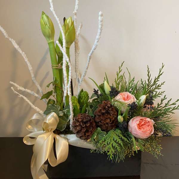 Floral arrangement with pink roses, amaryllis buds, and pinecones in a black box