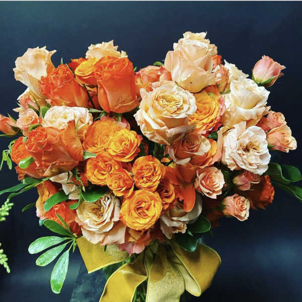 Bouquet of orange, peach, and white roses with a gold ribbon