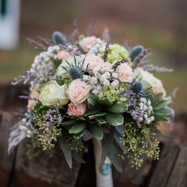 Bouquet of pale pink and white roses with blue thistle accents